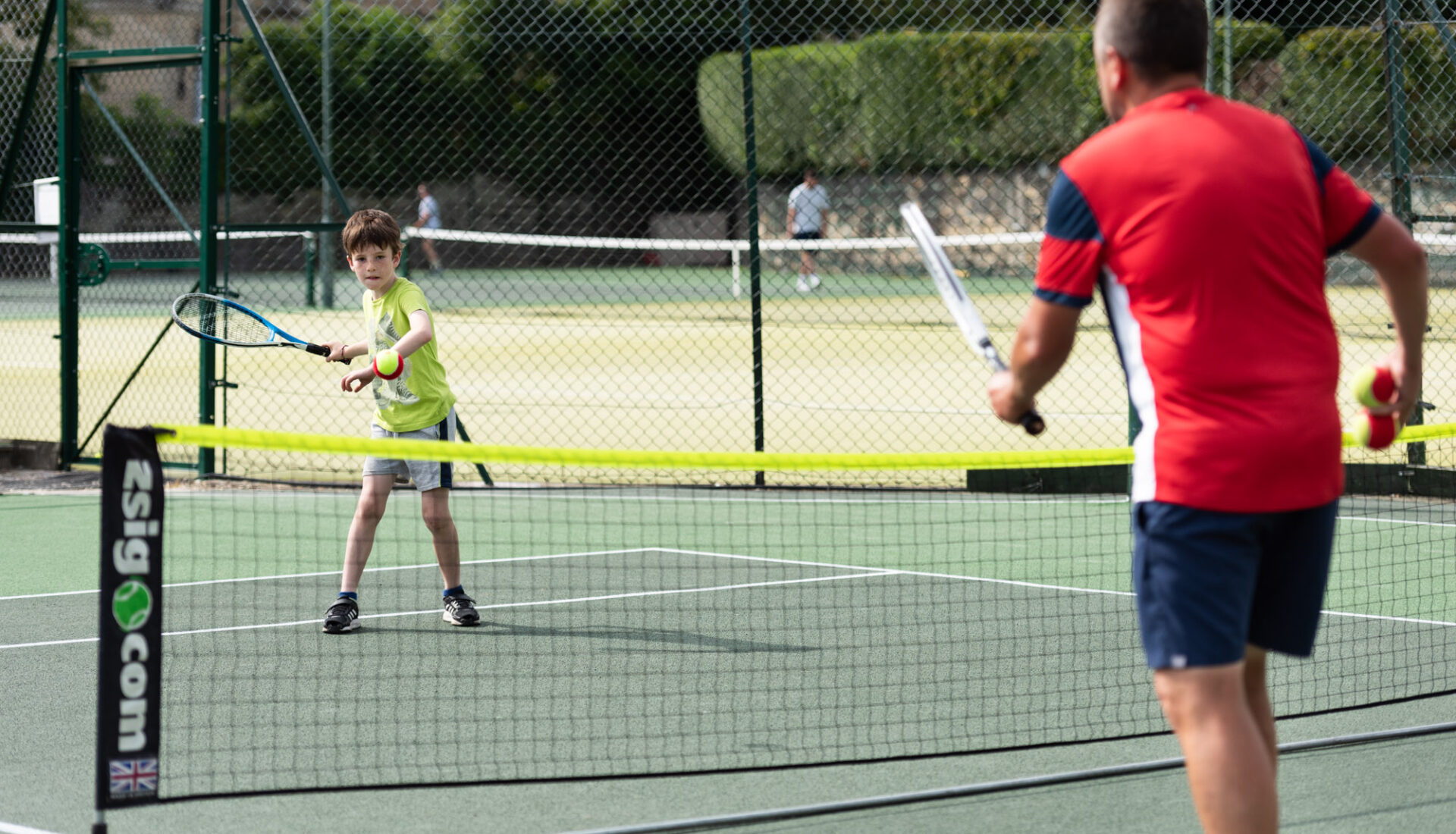 Tennis Lessons -Children's tennis lesson with Rich Little with child hitting forehand shot.
